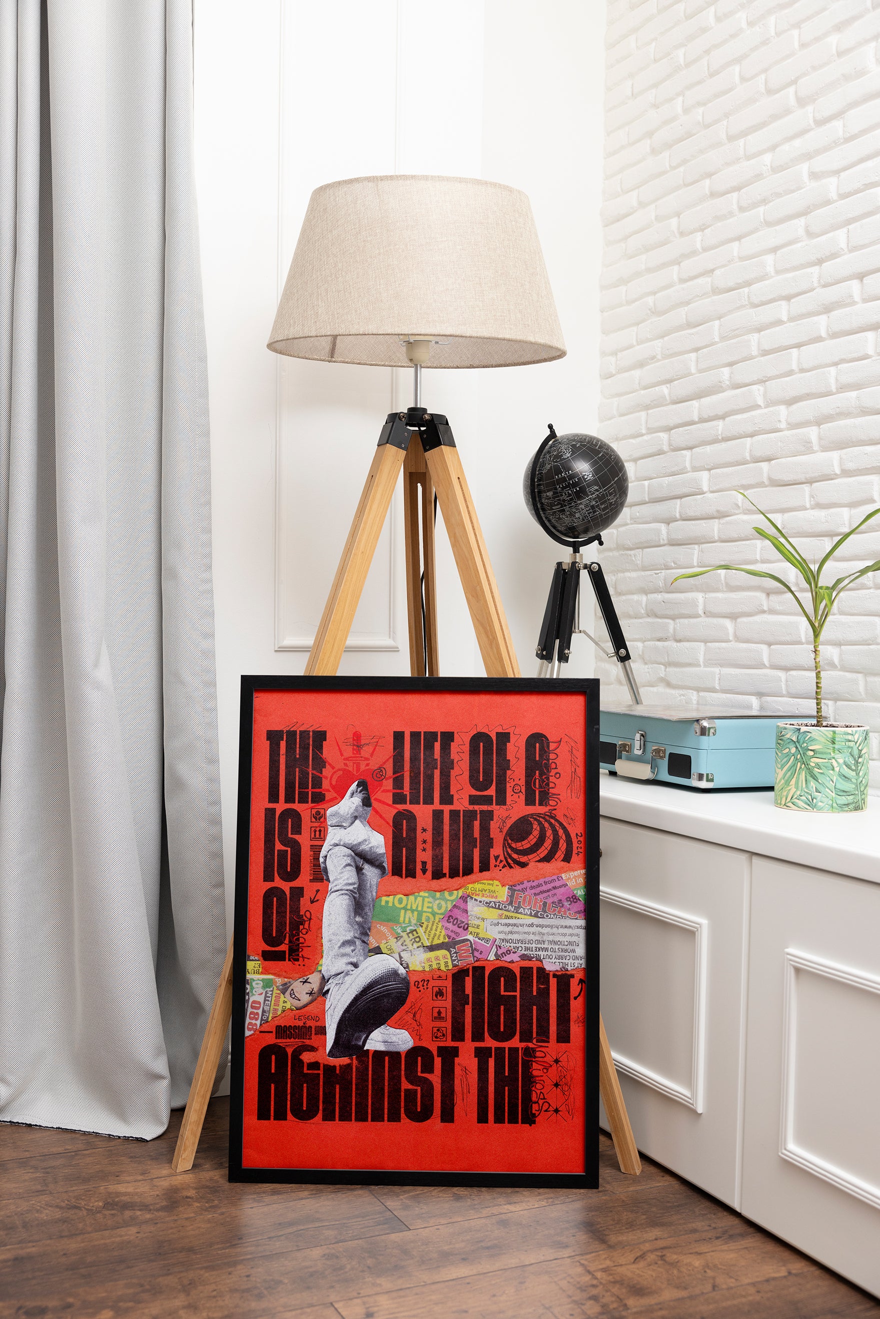 Life of a Designer poster with orange colors, displayed in a sleek black frame leaning against a lamp, styled with a globe in an adventure-themed room.